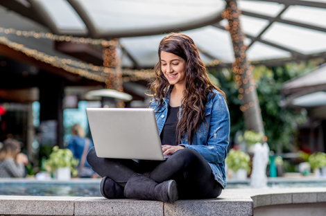 Woman sitting outside smiling at laptop