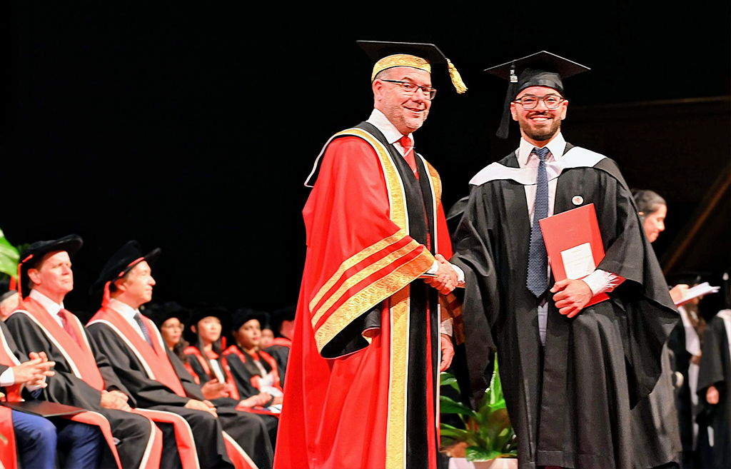 A student smiling and shaking hands with the Chancellor at his graduation
