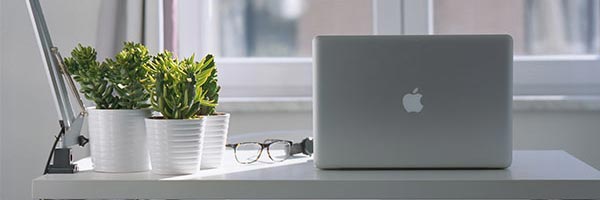 a macbook laptop sitting next to a pair of glasses and few potplants on a white desk
