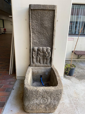 a stone sculputure with four human figues above a squared well