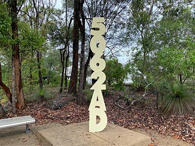 Steel sculpture of numbers and letters 5062AD aligning vertically on a concrete next to scrubs and trees