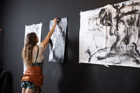 A student hanging drawing works on the wall in QCA's drawing studio