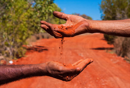 Red sand drizzling through two indigenous hands on a dirt road in the outback 