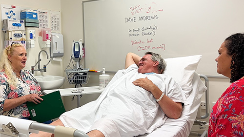man lying in hospital bed talking to two women