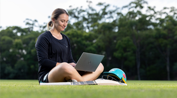 Female cricket player sitting outside with a laptop