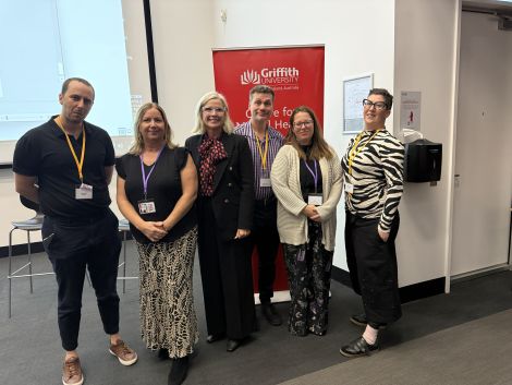 Six people wearing conference lanyards pose in front of a Griffith University Centre for Mental Health banner in a lecture theatre.
