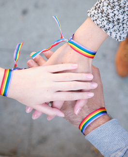 Three hands in a circle wearing rainbow bracelets
