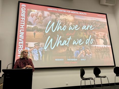 Presenter speaking at a lectern in front of a Griffith Centre for Mental Health presentation slide.