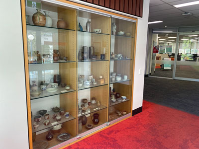 a beige-coloured wooden shelves with glass door filled with pottery