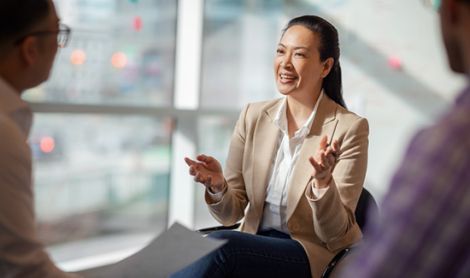 Multiracial Asian Hispanic Pacific Islander mature woman talking with colleagues in business office in meeting