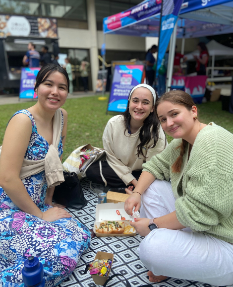 three students sitting on a picnic rug smiling