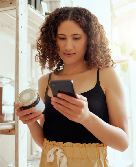 Woman shopping and holding jar whilst researching on phone 