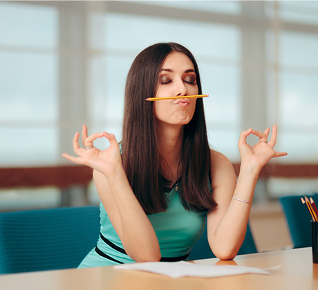 image of a female staff sitting at her office desk and holding a pencil between her nose and mouth