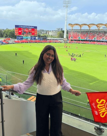 Indian student smiling at AFL game. 