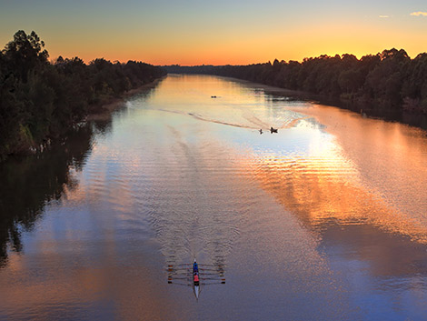 Sunrise over a river with rowers in the foreground