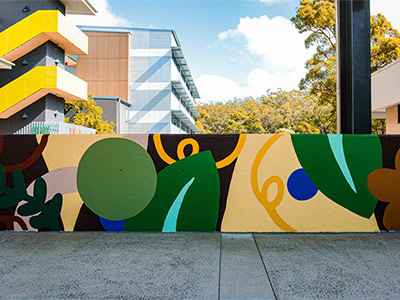 A colourful mural with greens, browns and yellows painted on a low concrete wall.