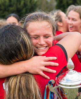 Two females hugging after winning a sport tournament with trophy